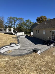 Paver patio using 24 x 24 Cambridge slabs shown in a Limestone Quarry Blend. Retaining wall was built using Cambridge Omega wall blocks shown with a Coal Platinum Smooth strip. Stairs are biult with Cambridge Crusader caps in the color Coal.