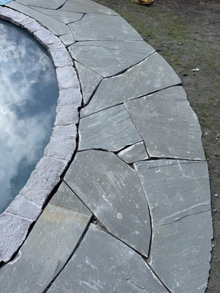 Pool coping shown in Nicolock Belvedere engineered wall stone in the color York Brown . Pool patio laid using natural irregular bluestone slabs.