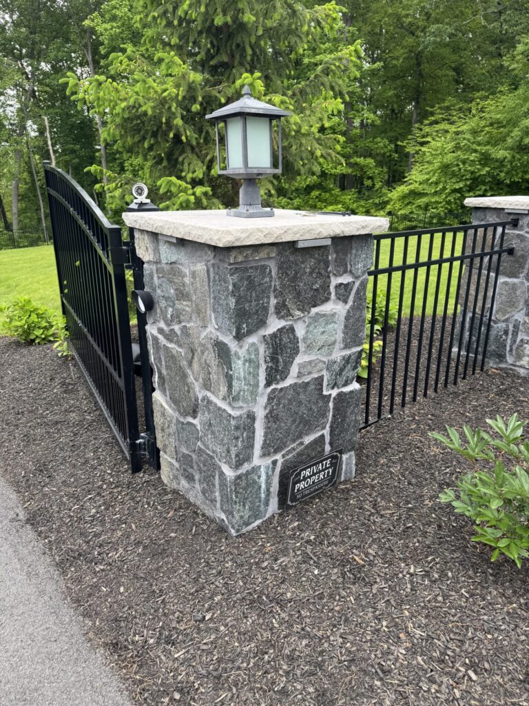 Pillars are made of R-Stone Mosaic veneer in the color Nantucket Blue capped with a Limestone topper. These are accompanied by aluminum fencing and gates that are controlled by American Armor Automation.