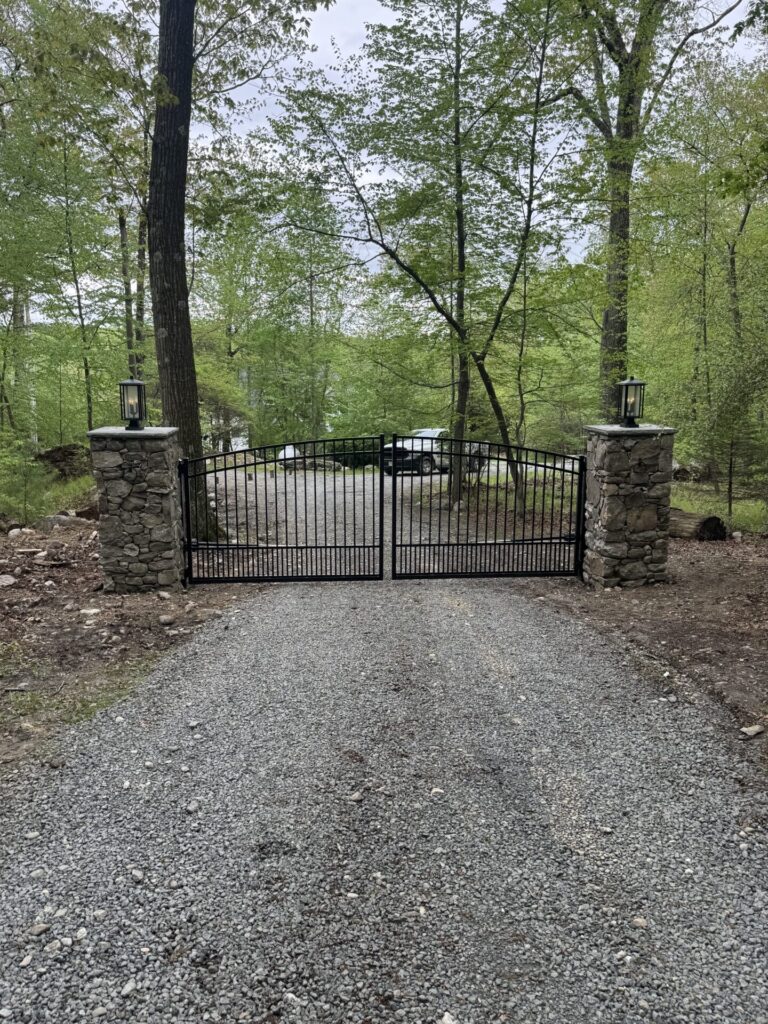 Estate gate pillars built with flagstone found onsite capped with a bluestone slab. The Interstate aluminum arched estate gate is adorned with puppy pickets and controlled by American Armor Automation.