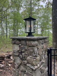 Estate gate pillars built with flagstone found onsite capped with a bluestone slab. The Interstate aluminum arched estate gate is adorned with puppy pickets and controlled by American Armor Automation.