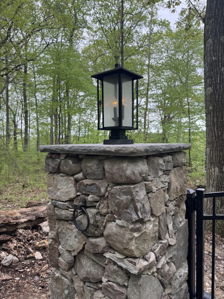 Estate gate pillars built with flagstone found onsite capped with a bluestone slab. The Interstate aluminum arched estate gate is adorned with puppy pickets and controlled by American Armor Automation.