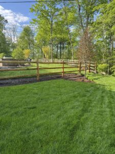 Round cedar three-rail fence with black welded wire mesh.