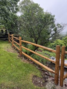 Round cedar three-rail fence with black welded wire mesh.