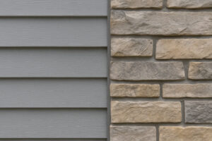 Close-up of gray vinyl siding paired with multi-toned stone veneer, showing a cohesive exterior material combination with complementary textures and undertones.