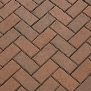 Close-up of a herringbone paver pattern showing interlocking reddish-brown bricks arranged at a 45-degree angle.