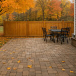 Backyard patio with paver stones, black metal furniture, and wooden privacy fence surrounded by fall foliage in a North Jersey suburban home.